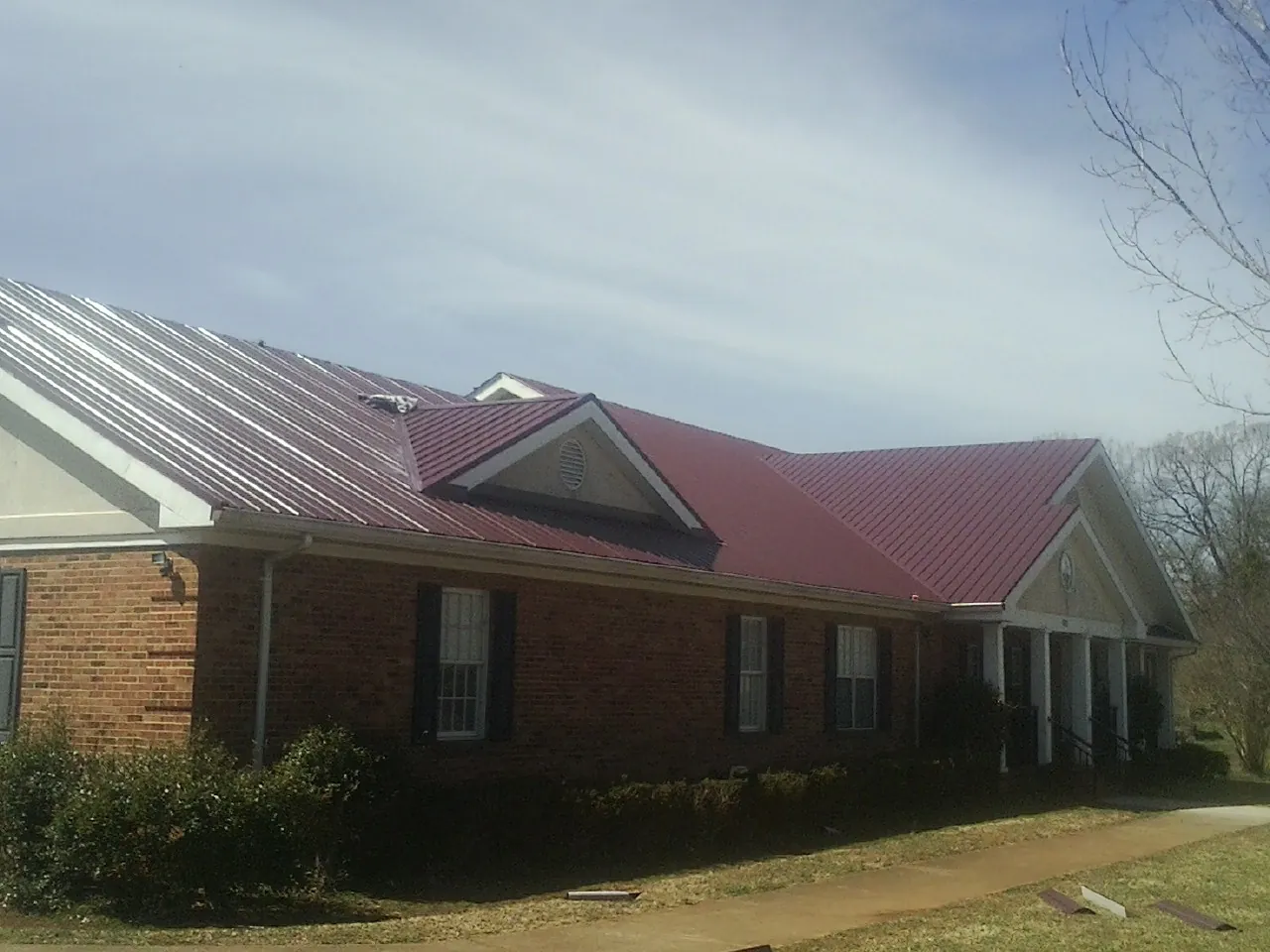 Red metal roof with gabled entries on a long brick building, from a Hail Damage Roof Repair job in Milan